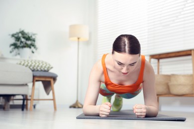 Photo of Young woman in sportswear doing plank exercise at home. Space for text