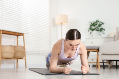 Photo of Young woman in sportswear doing plank exercise at home. Space for text