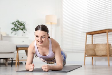 Photo of Smiling woman in sportswear doing plank exercise at home. Space for text