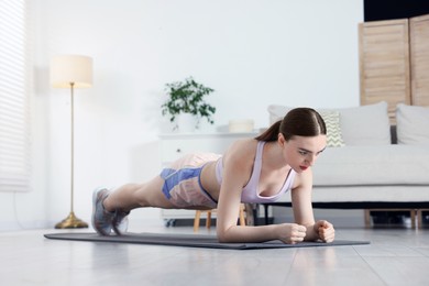 Photo of Young woman in sportswear doing plank exercise at home