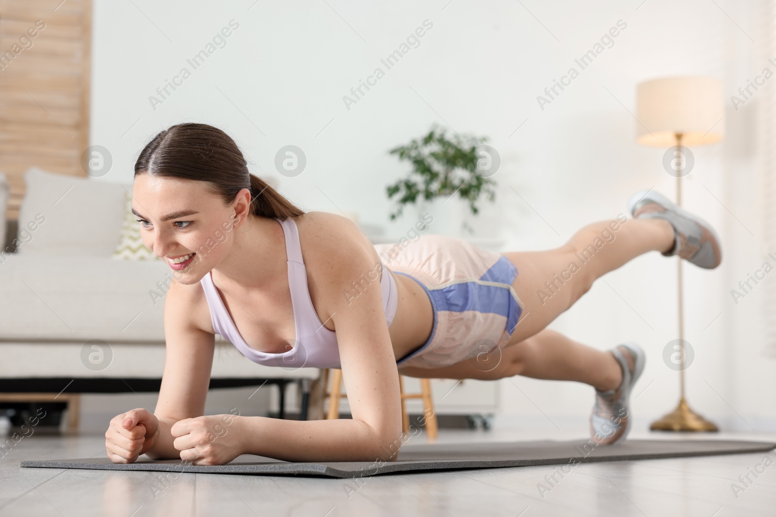 Smiling woman in sportswear doing plank exercise at home Photo of Smiling woman in sportswear doing plank exercise at home