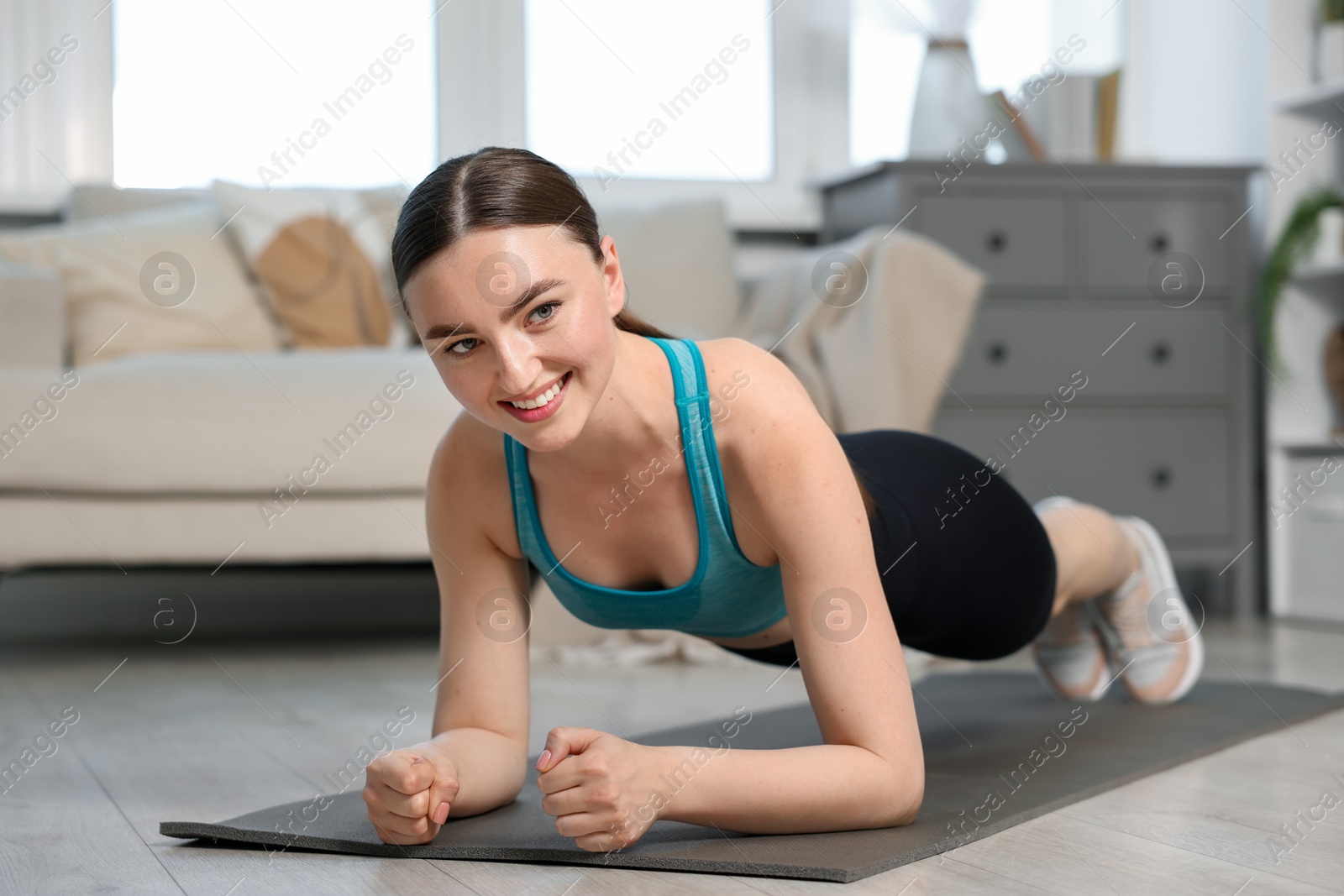 Smiling woman in sportswear doing plank exercise at home Photo of Smiling woman in sportswear doing plank exercise at home