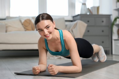 Photo of Smiling woman in sportswear doing plank exercise at home