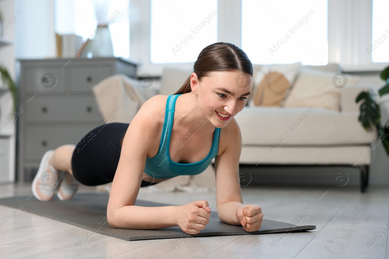 Smiling woman in sportswear doing plank exercise at home Photo of Smiling woman in sportswear doing plank exercise at home