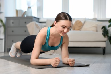 Photo of Smiling woman in sportswear doing plank exercise at home