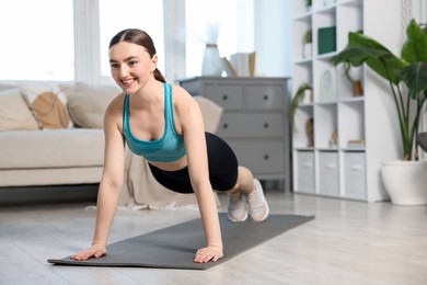 Photo of Smiling woman in sportswear doing plank exercise at home