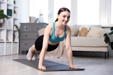 Photo of Smiling woman in sportswear doing plank exercise at home