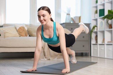 Photo of Smiling woman in sportswear doing plank exercise at home