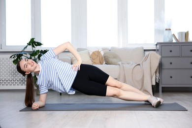 Photo of Smiling sporty woman doing side plank exercise at home