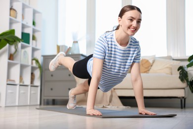Photo of Smiling sporty woman doing plank exercise at home, low angle view