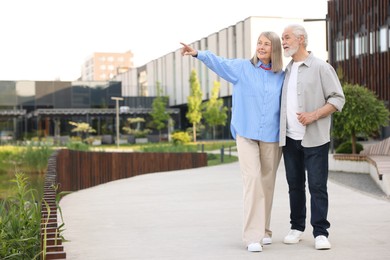 Photo of Lovely senior couple walking together on city street, space for text