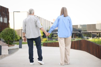 Photo of Lovely senior couple walking together on city street, back view