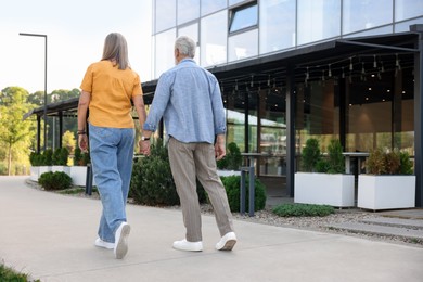 Photo of Lovely senior couple walking together near building outdoors, back view