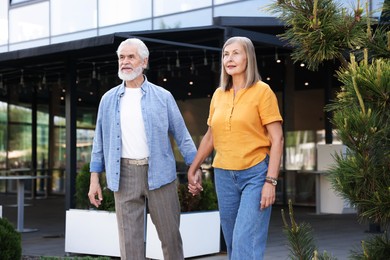 Photo of Lovely senior couple walking together near building outdoors
