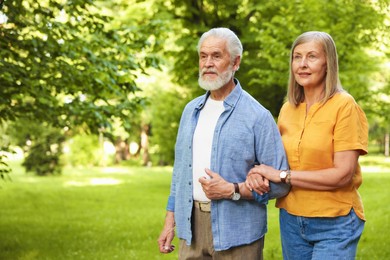 Photo of Lovely senior couple walking together in park, space for text