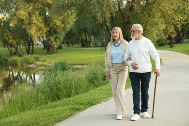 Photo of Lovely senior couple walking together near lake in park, space for text