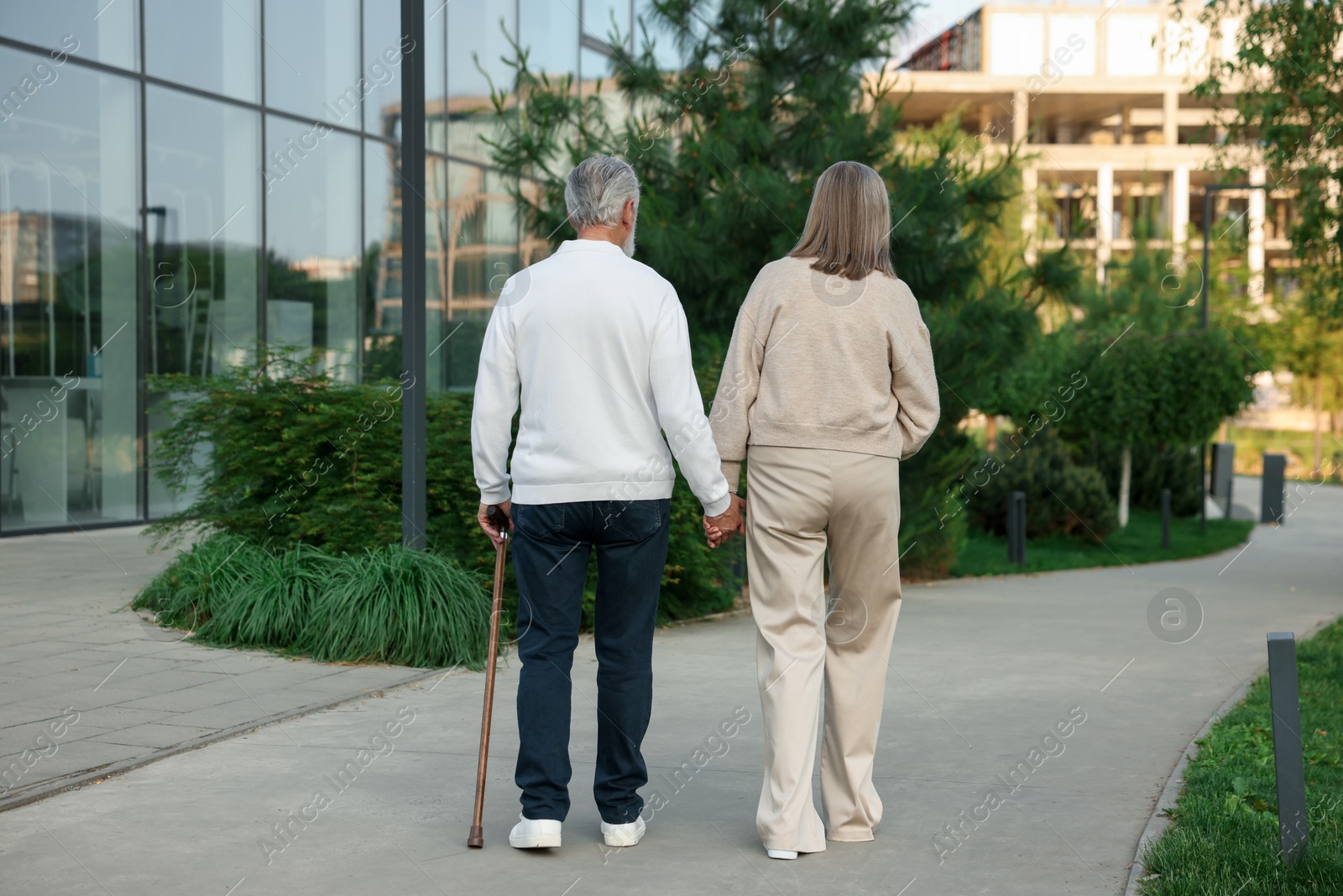 Lovely senior couple walking together near building outdoors, back view Photo of Lovely senior couple walking together near building outdoors, back view