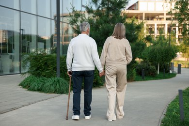 Photo of Lovely senior couple walking together near building outdoors, back view