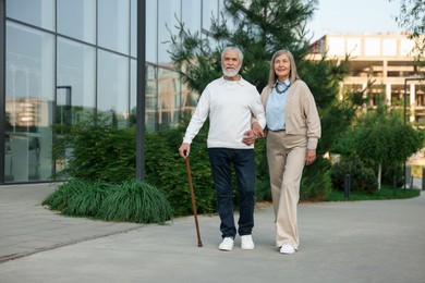 Photo of Lovely senior couple walking together near building outdoors