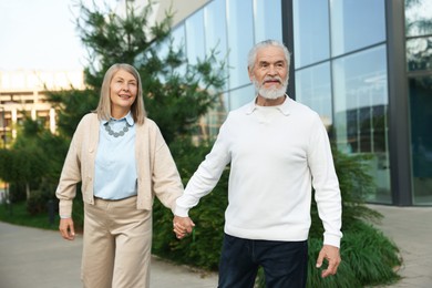 Photo of Lovely senior couple walking together near building outdoors