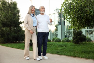 Photo of Lovely senior couple walking together near building outdoors, space for text