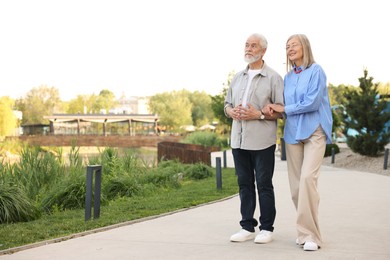 Photo of Lovely senior couple walking together in park, space for text
