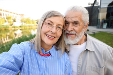Photo of Lovely senior couple walking taking selfie in park
