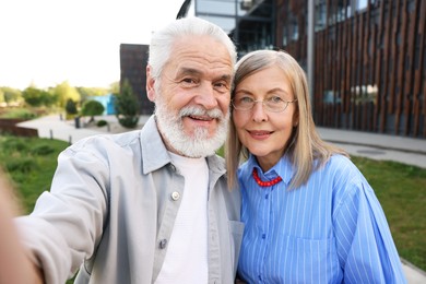 Photo of Lovely senior couple walking taking selfie in park