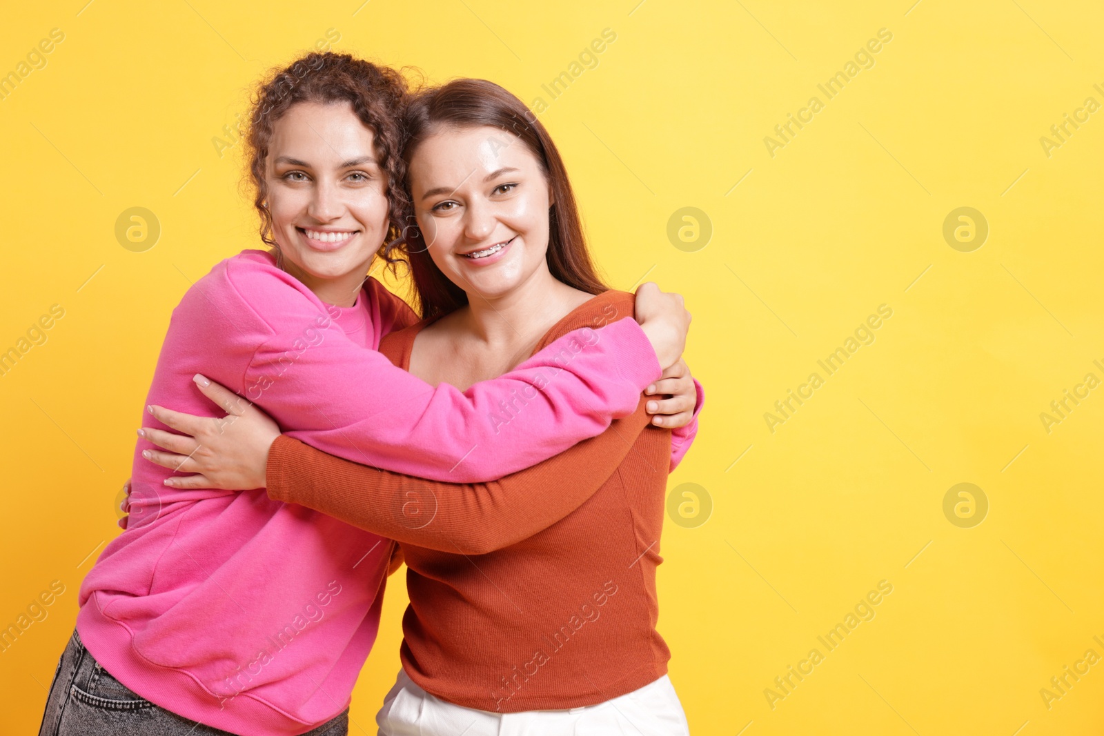 Friends hugging each other on orange background, space for text Photo of Friends hugging each other on orange background, space for text