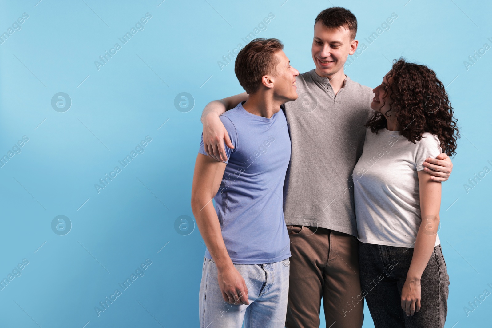 Three friends hugging on light blue background, space for text Photo of Three friends hugging on light blue background, space for text