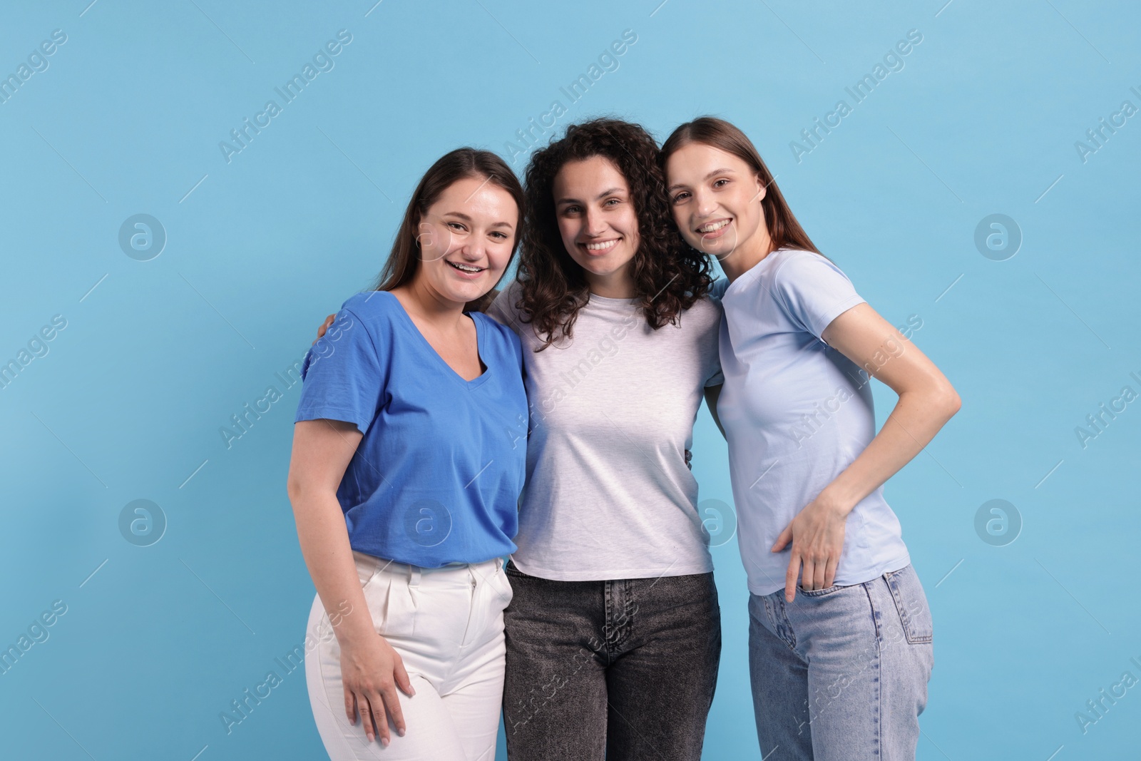 Three friends hugging on light blue background Photo of Three friends hugging on light blue background