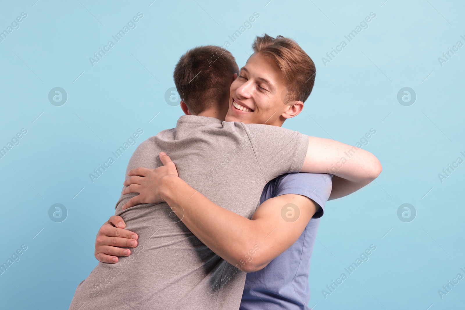 Two friends hugging on light blue background Photo of Two friends hugging on light blue background