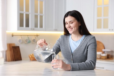 Photo of Woman pouring water into glass at white marble table in kitchen, space for text