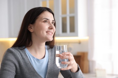 Photo of Woman with glass of water in kitchen, space for text
