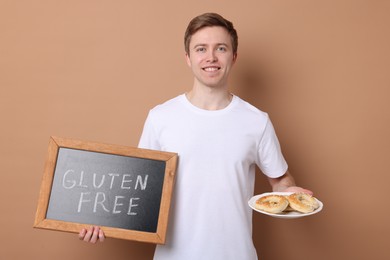 Photo of Man holding small chalkboard with text Gluten Free and pretzels on beige background