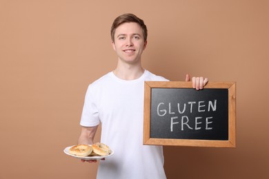 Photo of Man holding small chalkboard with text Gluten Free and pretzels on beige background