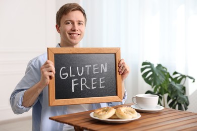 Photo of Man holding small chalkboard with text Gluten Free at wooden table indoors