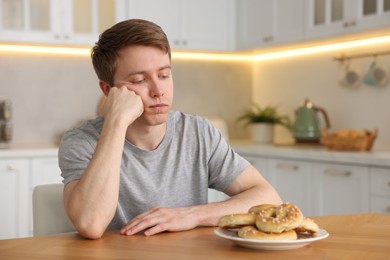Photo of Gluten free diet. Sad woman with pretzels at wooden table in kitchen