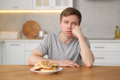 Photo of Gluten free diet. Sad woman with pretzels at wooden table in kitchen