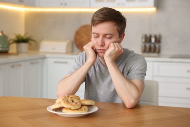 Photo of Gluten free diet. Sad woman with pretzels at wooden table in kitchen