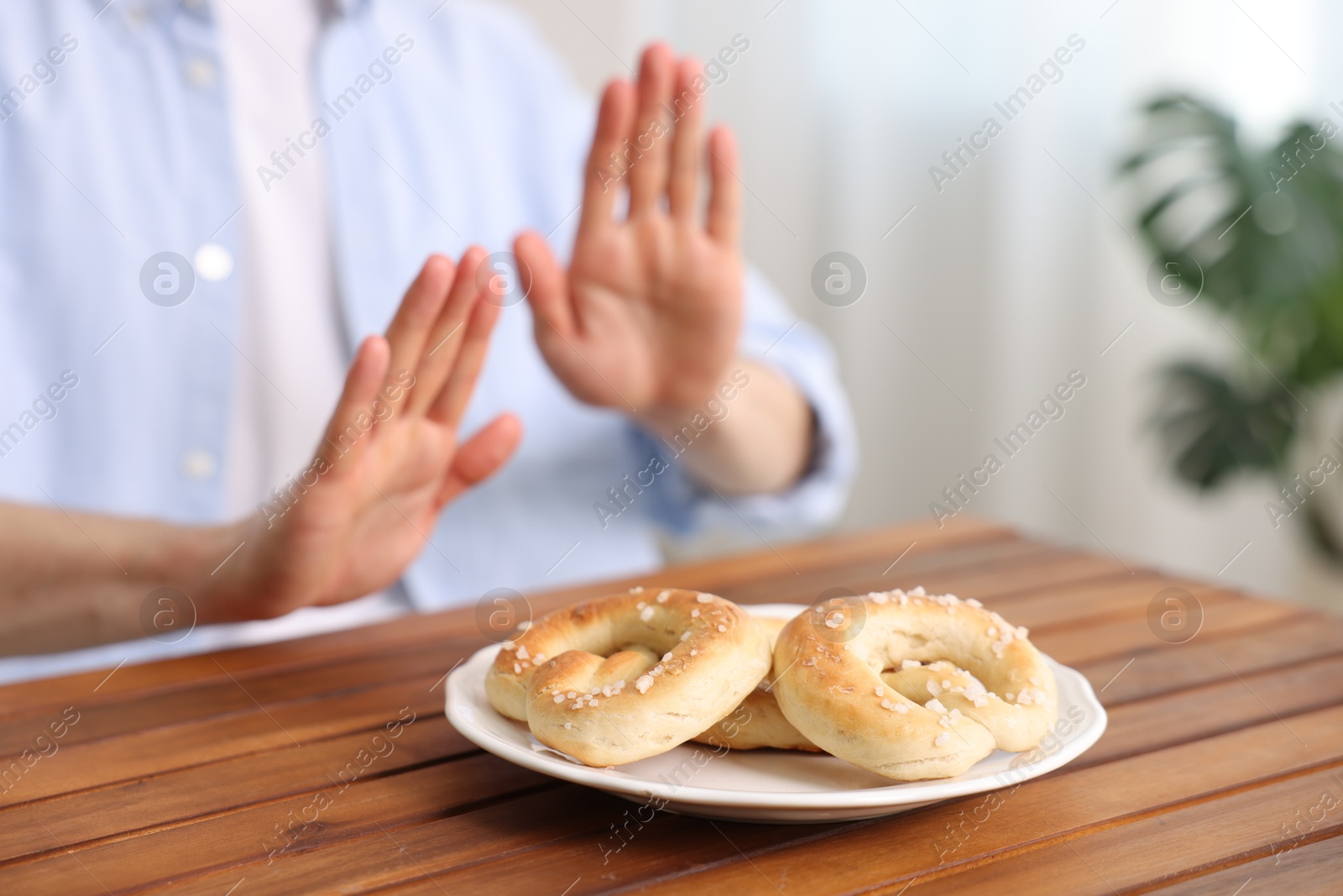 Gluten free diet. Man refusing from pretzels at wooden table indoors, selective focus Photo of Gluten free diet. Man refusing from pretzels at wooden table indoors, selective focus