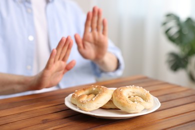 Photo of Gluten free diet. Man refusing from pretzels at wooden table indoors, selective focus