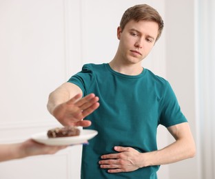 Photo of Gluten free diet. Man refusing from donut indoors, selective focus