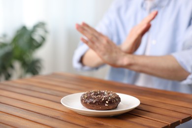 Photo of Gluten free diet. Man refusing from donut at wooden table indoors, selective focus
