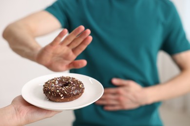 Photo of Gluten free diet. Man refusing from donut indoors, selective focus