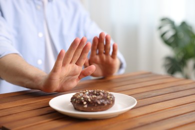 Photo of Gluten free diet. Man refusing from donut at wooden table indoors, closeup