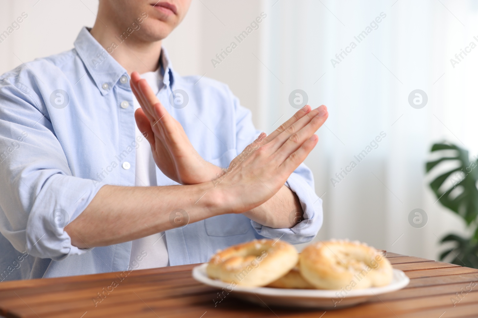Gluten free diet. Man refusing from pastries at wooden table indoors, closeup Photo of Gluten free diet. Man refusing from pastries at wooden table indoors, closeup