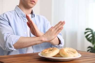 Photo of Gluten free diet. Man refusing from pastries at wooden table indoors, closeup