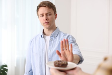 Photo of Gluten free diet. Man refusing from donut indoors, selective focus