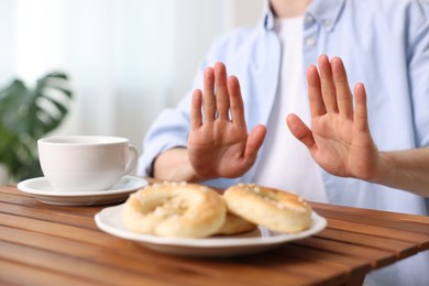 Photo of Gluten free diet. Man refusing from pastries at wooden table indoors, closeup